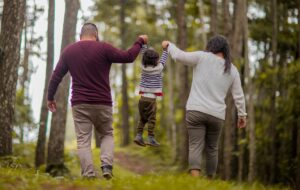 Father and mother swinging todler between them as they walk through a forest