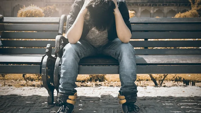 Man holding his head sat on a bench at a drug and alcohol rehab in Glasgow