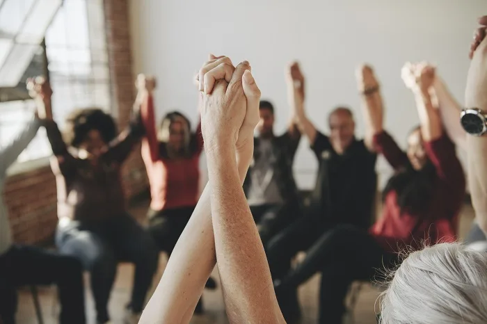 Peer support group holding raised hands at a drug and alcohol rehab centre in Manchester