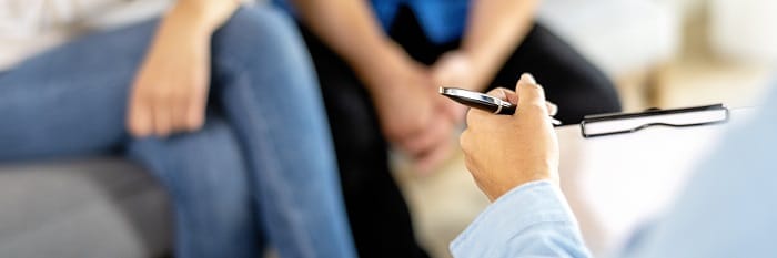 Therapist taking notes whilst speaking with a couple at a drug and alcohol rehab clinic in the West Midlands