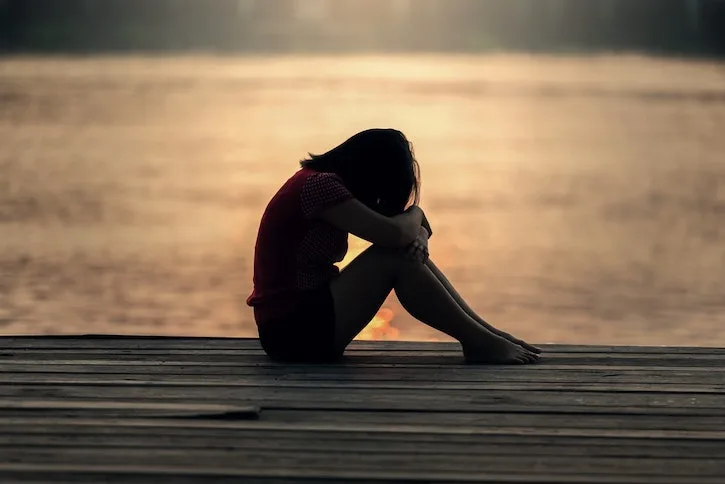 Woman holding her knees sat next to a lake at drug and alcohol rehab clinic addiction service in Middlesbrough