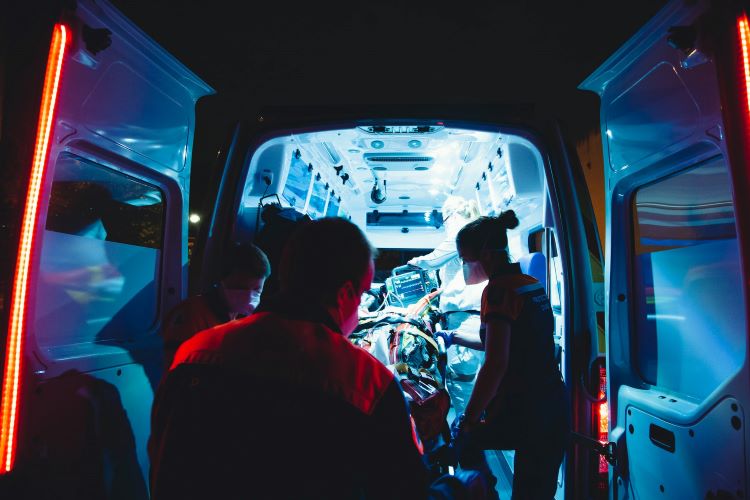 The inside of a lit ambulance on a dark night. Paramedics moving someone on a stretcher and administering overdose medication