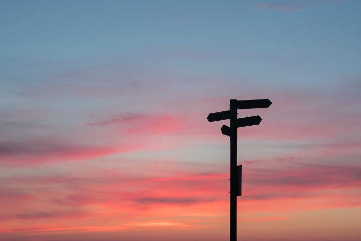 A multi-way signpost silhouetted against a pink sunset sky
