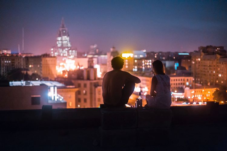 Two friends taking drugs, silhouetted against a city skyline