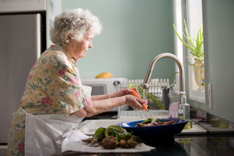 An elderly woman with a Fentanyl addiction washing carrots at a sink