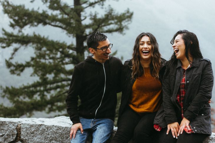 Three friends laughing. Behind them, a grey sky and tree