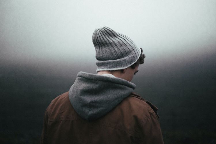 A man turning his back. He wears a woolly hat and the sky is grey