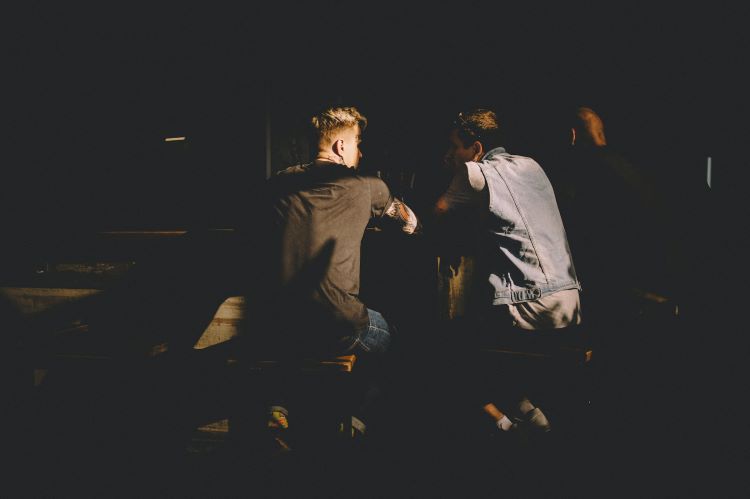 Two men with tattoos talking in a dark setting