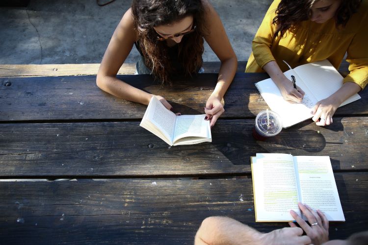 Three people at a wooden table, writing and reading