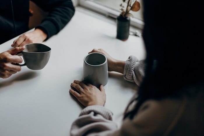 Two people drinking hot drinks and discussing long COVID