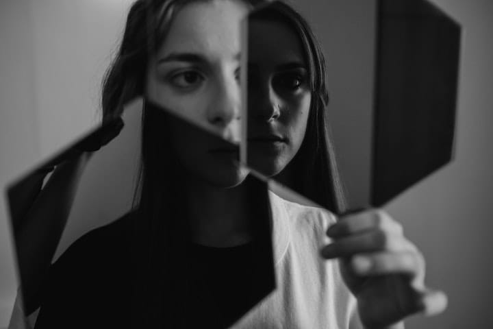 Black and white photo of a woman looking into several mirrors