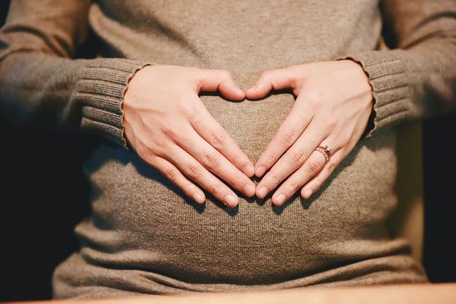 Pregnant person holding their belly and thinking about heroin addiction