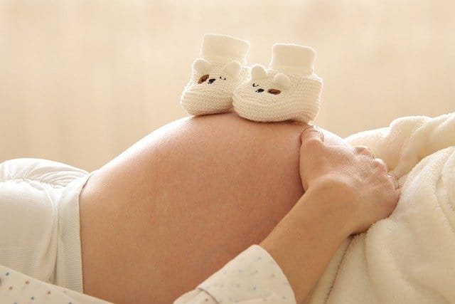 Pregnant person lying down with infant shoes on their belly