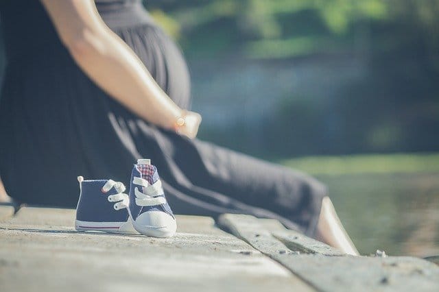 Pregnant person sat next to a pair of infant shoes and thinking about heroin addiction