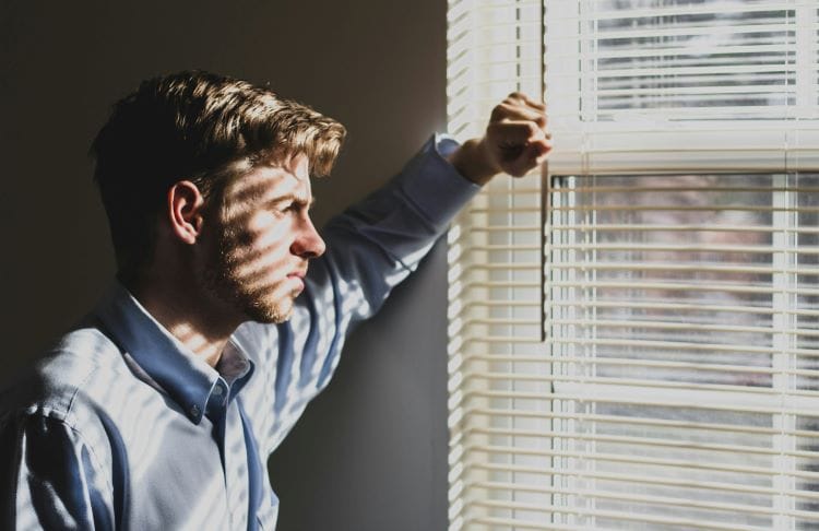 A man looking out of a window with sunlight coming through the blinds