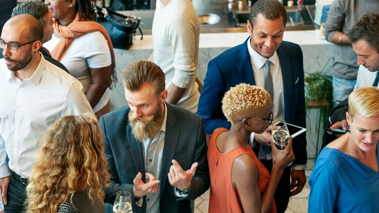 People dressed in formal attire, drinking from wine glasses and chatting